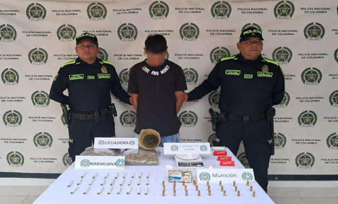 Dos policias con un hombre capturado en el medio, y estupefacientes en una mesa