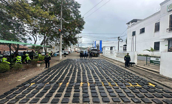 Persoa capturada al fondo, paquetes de marihuana en el piso organizados y patrullas de Policia alrededor 
