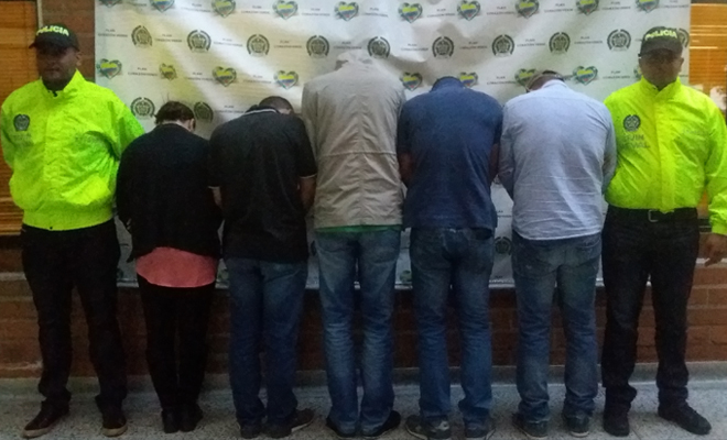 Cinco personas de espaldas son custodiadas por un policía de la SIJIN