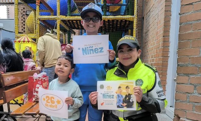 Una mujer policía acompañada de un niño y una niña con carteles que dicen 26 de abril día de la niñez.