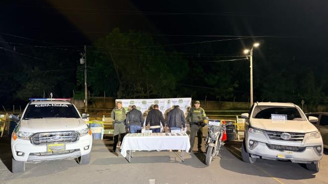 Dos policías al lado de dos hombre capturados con estupefacientes, un moto y una camioneta