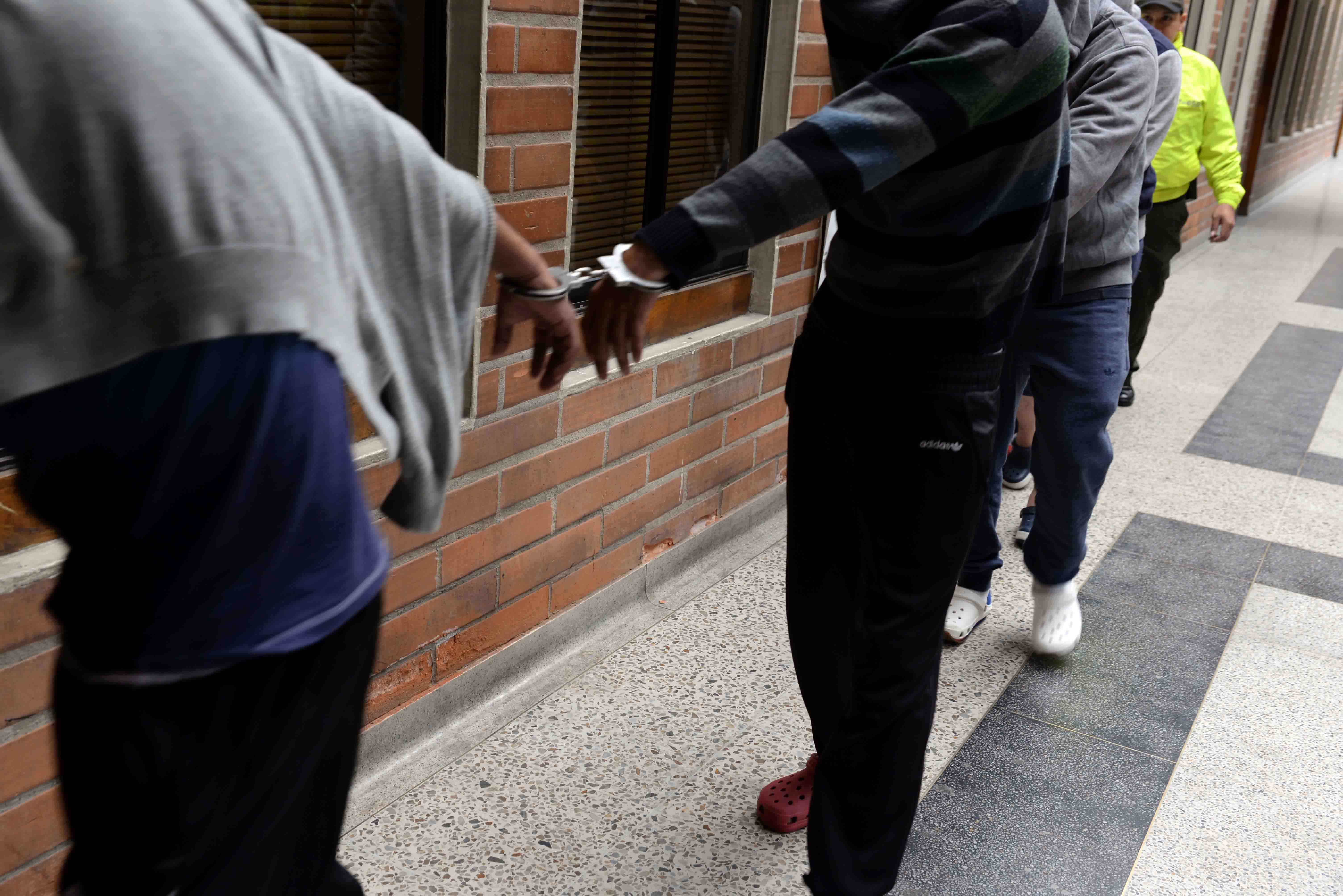 Cuatro hombres caminan esposados, un policía los custodia