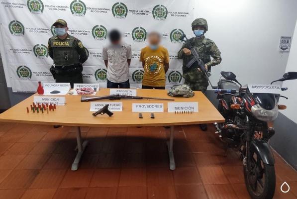 Dos personas capturadas-policías custodiando-armas de fuego incautadas